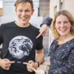 Ben Förtsch und Tina Teucher stehen nebeneinander. Zeigen auf das T-Shirt von Ben Förtsch mit der Erdkugel drauf