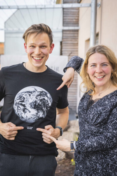 Ben Förtsch und Tina Teucher stehen nebeneinander. Zeigen auf das T-Shirt von Ben Förtsch mit der Erdkugel drauf